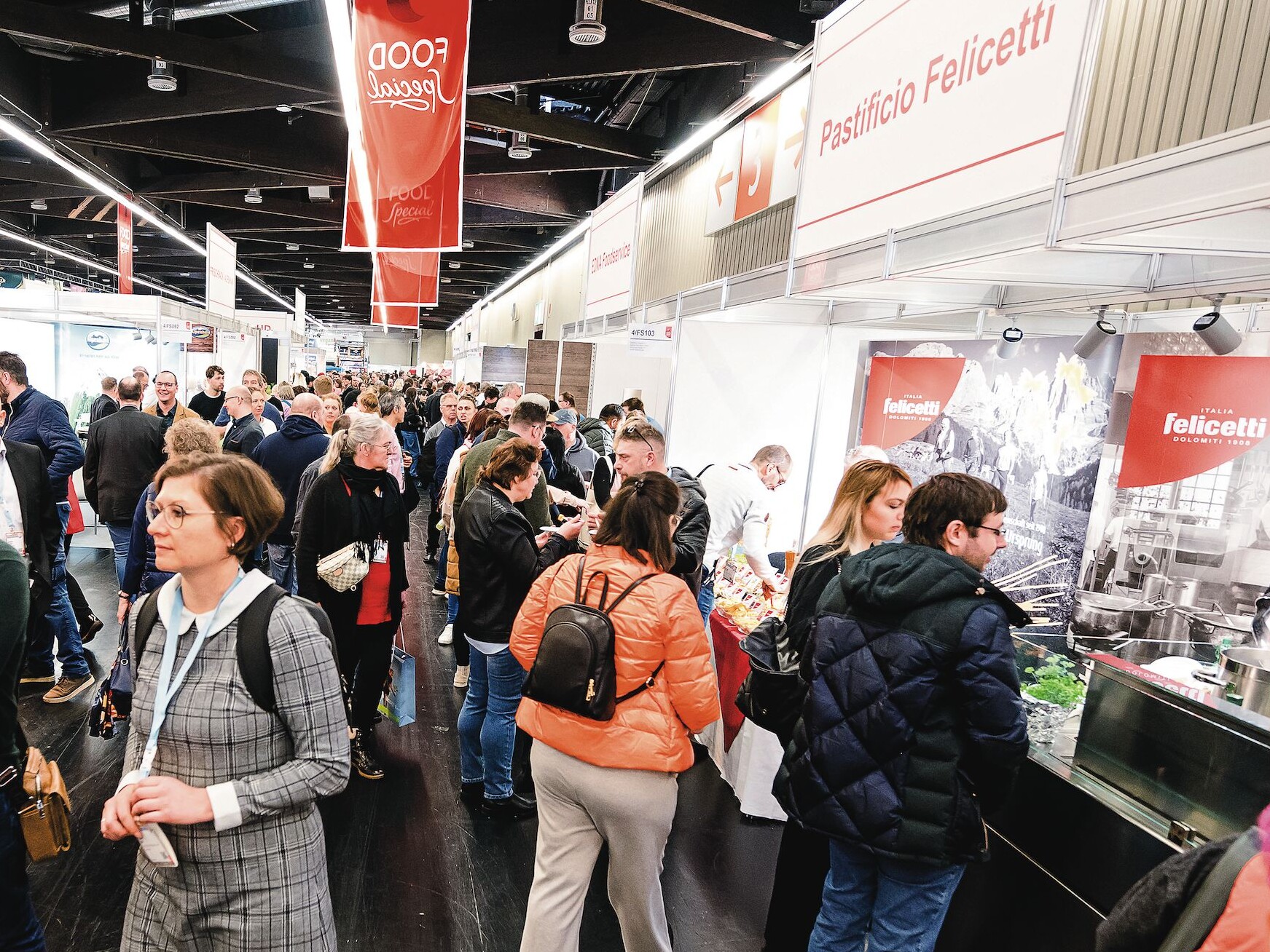 riationen Eine Gruppe von Menschen in einem Raum, darunter Männer und Frauen, die stehen und miteinander interagieren.